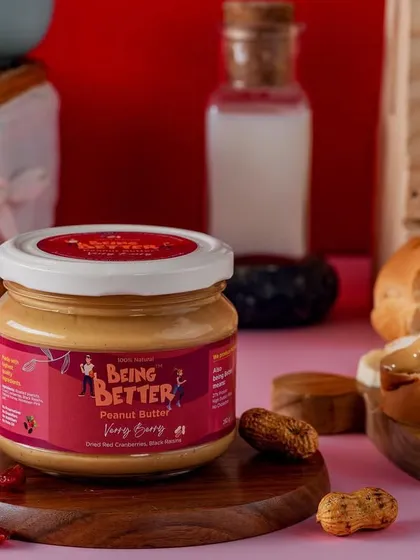 A cozy, picnic-style setup for Being Better's peanut butter. The checkered cloth and wooden board create a warm, inviting scene that suggests wholesome, family-friendly enjoyment.