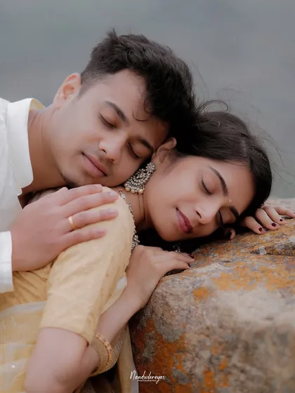 A serene portrait of a couple resting together on a rock, their eyes closed in a moment of shared peace.