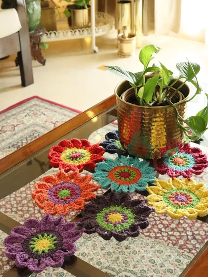 A vibrant collection of my flower-shaped crochet coasters scattered on a coffee table. Each one is a burst of colour, perfect for protecting surfaces during your coffee or tea breaks.