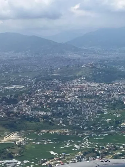 An aerial view of the Kathmandu Valley as we fly into Nepal. The landscape is a patchwork of towns and green fields, nestled between the hills.