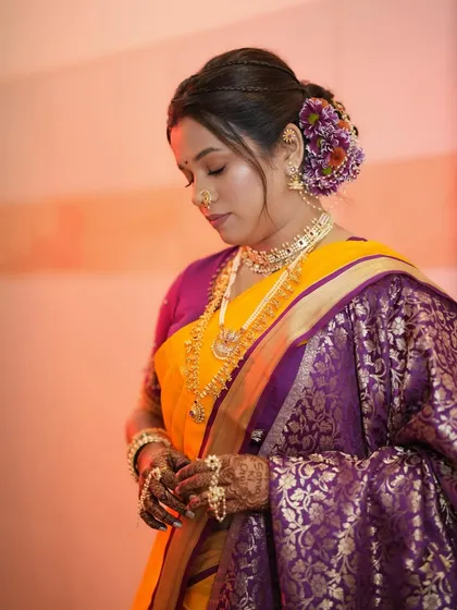 A serene moment captured. The bride looks down, showcasing her soft eye makeup and the intricate details of her floral hair arrangement.