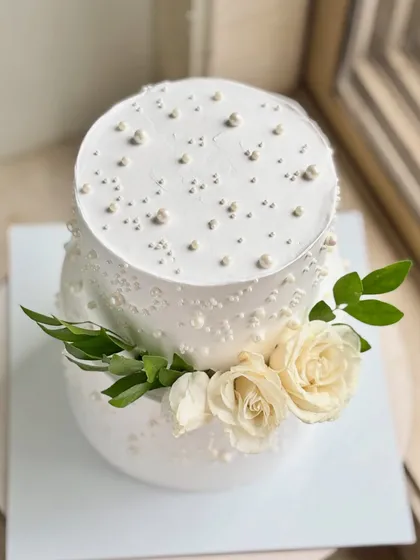 An overhead view showing the delicate pearl work on the top tier of this elegant white cake. The placement of the fresh roses adds a touch of natural beauty.