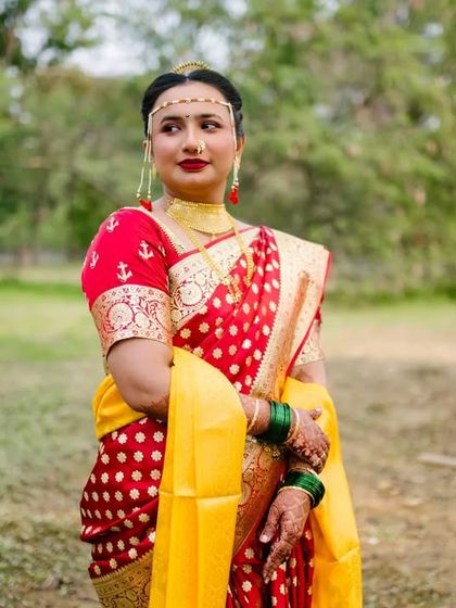 A portrait of the bride in her striking red and yellow wedding saree, looking elegant and poised in a natural outdoor setting.