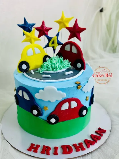 A simple and sweet car-themed cake for Hridhaan's 4th birthday, with colorful cars driving on a grassy hill under a blue sky.