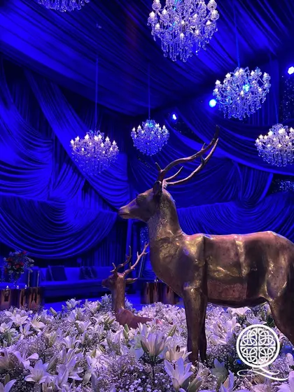 For this 'Chandni Raatein' or 'Moonlit Nights' theme, I used a deep royal blue for the drapery. The space is filled with statues of deer amidst a field of white lilies, all under the glow of crystal chandeliers, creating a serene and mystical forest scene.