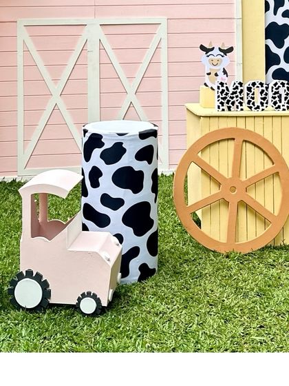 A close-up of the farm decor, featuring a pink tractor, a cow-print pedestal, and a large barn door backdrop.