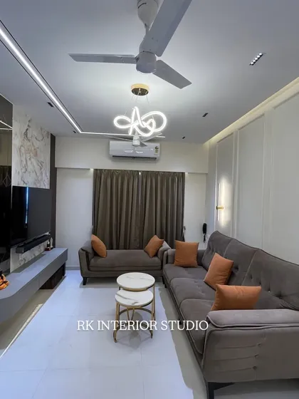 This living room features a floating TV unit with a marble-finish back panel and a mirrored wall that makes the space feel larger. The modern chandelier and profile lights in the ceiling add to the luxurious ambiance.