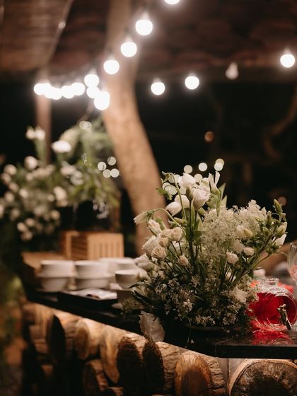 A rustic bar setup for the "Into the Woods" dinner, with a log base and simple white floral arrangements.