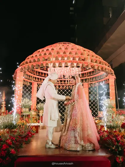 A union blessed by a thousand bells. This heritage-inspired bell mandap was designed to be both grand and sacred, with the couple framed by the structure's powerful symbolism and the warm glow of the evening.