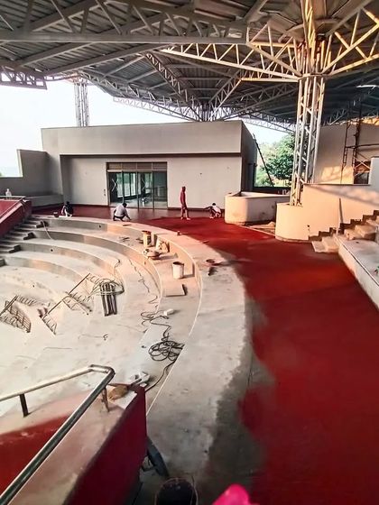 A wide shot of the TAPMI amphitheater under construction, before the installation of the bamboo parasols, revealing the scale of the concrete and red oxide work.