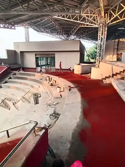 A wide shot of the TAPMI amphitheater under construction, before the installation of the bamboo parasols, revealing the scale of the concrete and red oxide work.