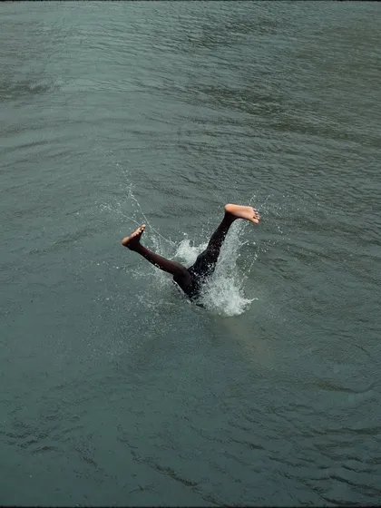 The moment of impact as a diver's legs disappear into the water. This abstract and energetic shot focuses on the splash and the motion, conveying the simple thrill of a monsoon dive.