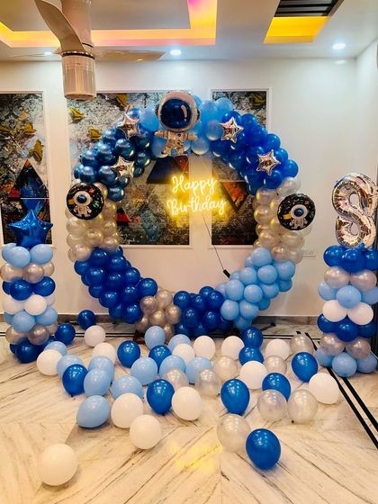 An exciting space theme birthday decoration featuring a ring backdrop filled with blue and silver balloons, astronaut cutouts, and star and planet details.
