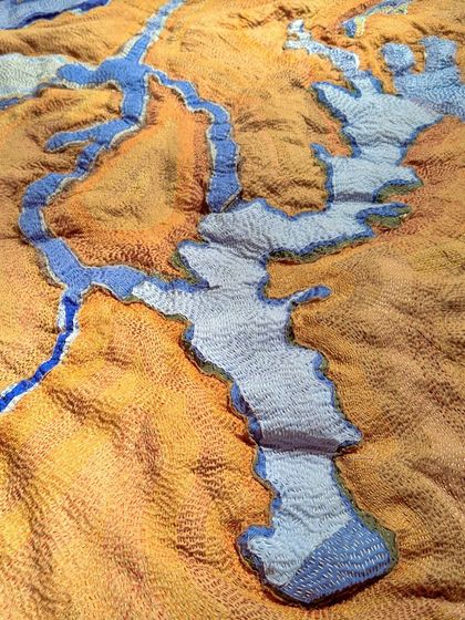 'A Piece of Earth', a textile artwork from our 'Cu+Fibers' exhibition. This piece uses kantha stitching and varied fiber textures to create a topographical map, abstracting a landscape into a tactile surface.
