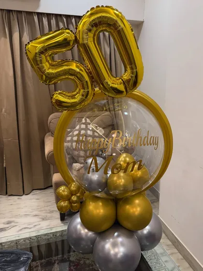 Celebrating the big 5-0! This custom standing balloon bouquet features giant gold '50' foil balloons and a personalized bubble balloon wishing Mom a happy birthday in a luxe gold and silver theme.