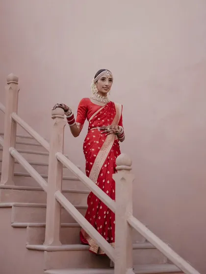 A graceful portrait of the bride in her red silk saree, descending the stairs of the palace. This shot has a timeless, classic feel, highlighting the elegance of the bride and the venue.