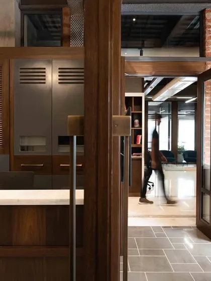 A glimpse of the reception area and entryway at the Prodigy Investment Management office. The design combines dark wood cabinetry with exposed brick and tiled flooring, creating a welcoming yet professional first impression.