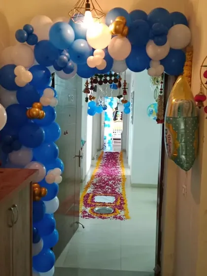 A grand entrance for a "Welcome Baby" celebration at home. A blue and white balloon arch leads into a hallway with a beautiful flower petal runner on the floor.