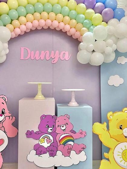 A close-up of a colorful rainbow and Care Bears themed party, with a pastel rainbow balloon arch and cute character cutouts.