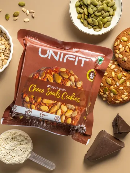 A packet of choco-seed whey protein cookies, styled with a scoop of whey powder and seeds.