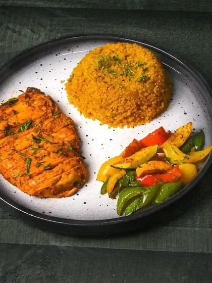 A healthy meal of chicken shish taouk served with quinoa and colorful bell peppers. The dark background and simple plating give it a professional and clean aesthetic.