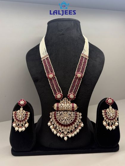 This majestic rani haar features a large, ornate pendant with maroon stones and pearl drops, designed to make a statement.