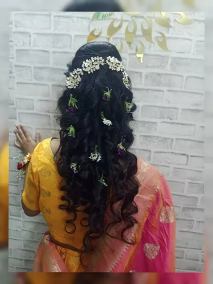 This photo highlights the hairstyling for a Haldi ceremony look. The student has created soft, cascading curls adorned with a 'gajra' style hairpiece and scattered fresh flowers, a popular hairstyle for Indian pre-wedding events.