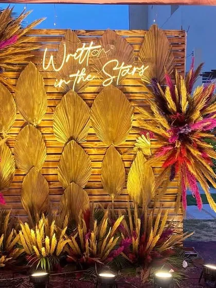 A great photo booth is essential for making memories. For this event, I designed a 'Written in the Stars' backdrop using a wooden wall, golden dried palm leaves, and colorful floral bursts to create a modern and stylish spot for photos.