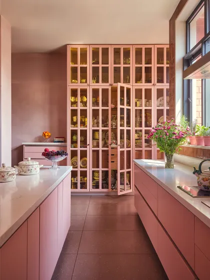 In a home where every room tells a story, the kitchen speaks in shades of rose. Tall, glass-fronted cabinets display collected china like a private museum, blending utility with personal history.