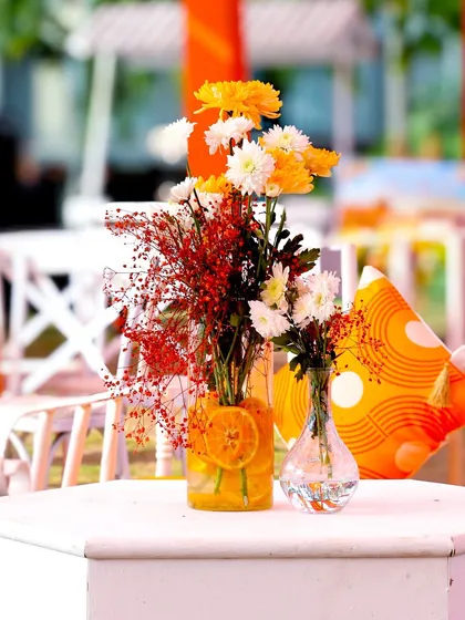 A beautiful tabletop centerpiece combining yellow and white flowers with red baby's breath. Sliced oranges in the vase add a creative, thematic touch.