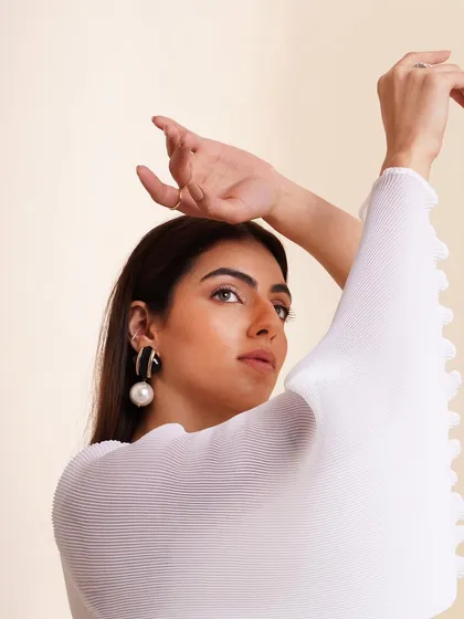 A close-up shot focusing on a white pleated top with bell sleeves. The styling with statement pearl earrings adds a touch of elegance and sophistication.