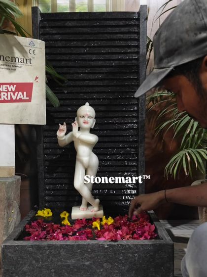An artisan carefully adds flower petals to the water of the Kanha Ji fountain, preparing it for display.