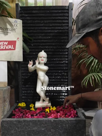 An artisan carefully arranges flowers in the basin of the Kanha Ji fountain. This piece combines the divinity of a hand-carved Krishna statue with the modern aesthetic of a granite wall fountain.