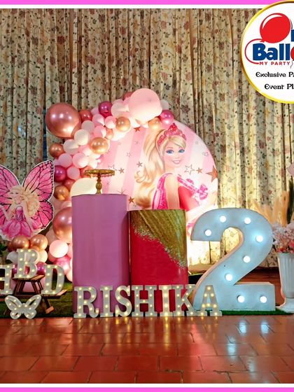 A pretty-in-pink Barbie-themed second birthday. The setup includes a Barbie backdrop, a large light-up number '2', and a 'RISHIKA' marquee.