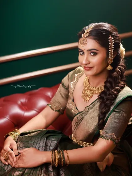 A modern bridal portrait with a classic feel. The bride's confident look, combined with the rich green saree and the elegant setting of a red leather sofa, creates a sophisticated and stylish image.
