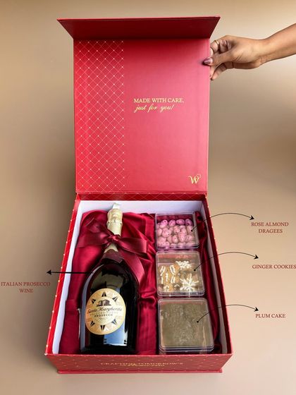 A detailed look inside the "Wishit Signature Box 2.0". This image breaks down the contents: Italian prosecco wine, rose almond dragees, ginger cookies, and plum cake, all elegantly arranged.