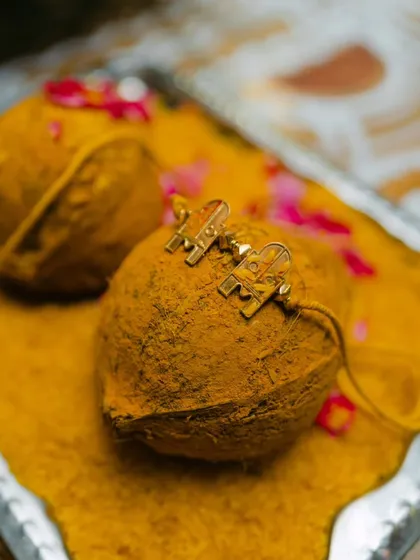 A close-up of traditional Hindu wedding items, with personalized cufflinks resting on a coconut covered in turmeric. This shot captures the unique and personal details of the ceremony.