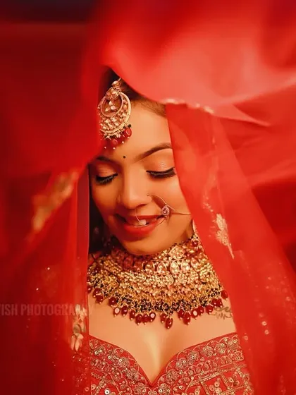 A candid bridal portrait capturing a genuine smile as the red veil flows around her. The motion in the veil adds a dynamic and artistic element.