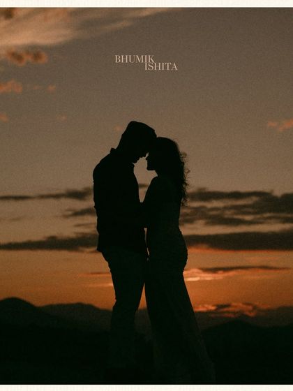 A classic sunset silhouette in the Georgian mountains. The couple is framed against the warm, orange sky, creating a simple, beautiful, and deeply romantic pre-wedding image.