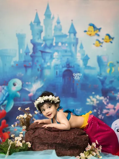 Made of magic, waves, and a splash of sparkle. A little mermaid relaxes on a rock in front of her underwater castle.