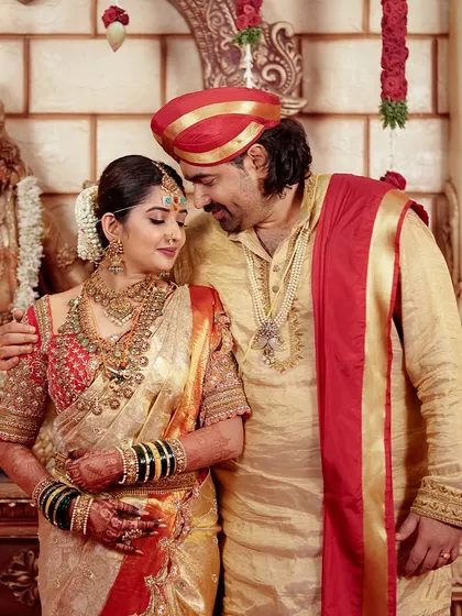 A regal portrait of the couple in a temple-like setting, showcasing their magnificent traditional wedding attire and the grandeur of the occasion.