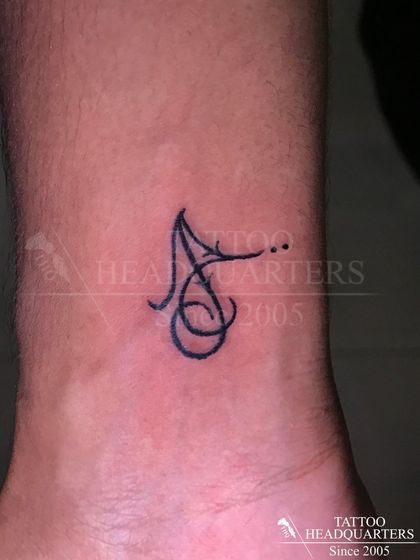 A stylized initial "A" tattoo on the wrist, created with a single flowing line.