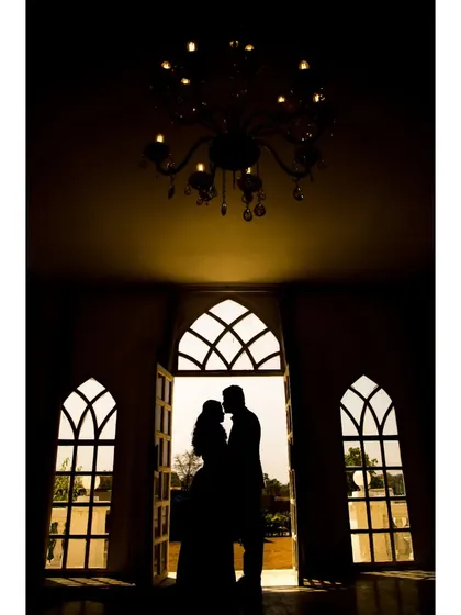 A classic silhouette of the couple framed by ornate windows and a chandelier. This pre-wedding photo has a timeless, grand, and romantic feel.