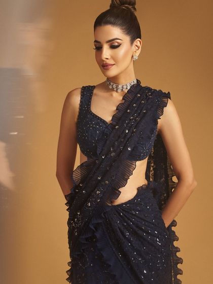 A client in a shimmering navy blue saree, her makeup is elegant with a top knot bun and defined eyes.