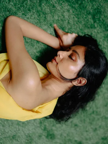 An overhead shot of a model in yellow fabric lying on green turf. The color contrast and serene pose create a visually striking and peaceful image.