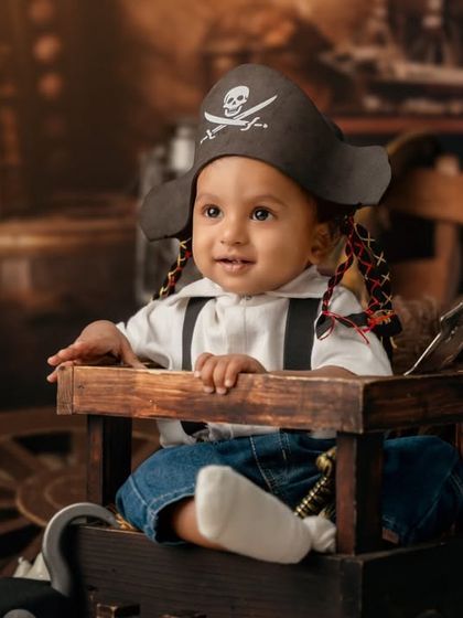 Ahoy, little pirate. This toddler is all smiles in his pirate hat, ready to set sail on a sea of imagination in this detailed, rustic setup.