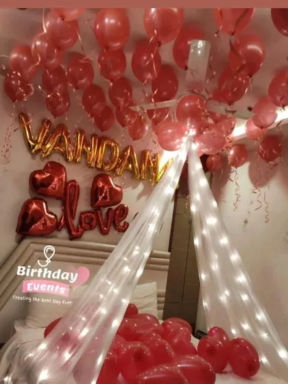 A bold and romantic room setup in all red. We used a fairy light canopy, personalized the wall with "Vandana" and "Love" foil balloons, and filled the bed with heart-shaped balloons.