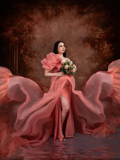 An artistic and dramatic portrait featuring a flowing peach gown. The fabric is tossed to create beautiful wings, and the water reflection adds a magical, ethereal quality to the image.