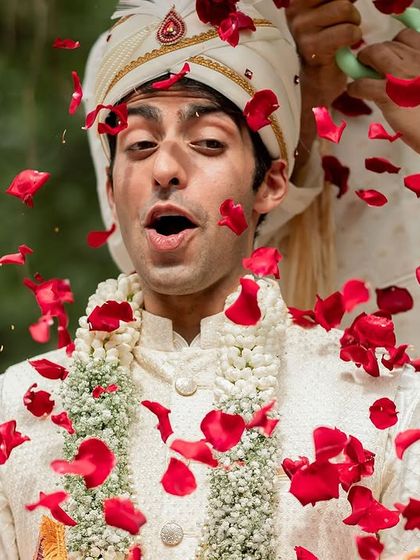 A groom's joyful reaction as he is showered with red rose petals during the 'baraat' or wedding procession.