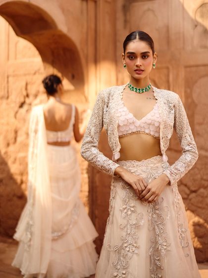 This image demonstrates layered styling with a delicate embroidered jacket over a bralette and lehenga skirt. The look is modern, chic, and perfect for a sangeet or reception.